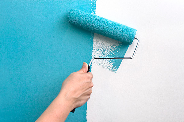 Painter applying teal blue paint on a wall with a roller for a smooth finish.